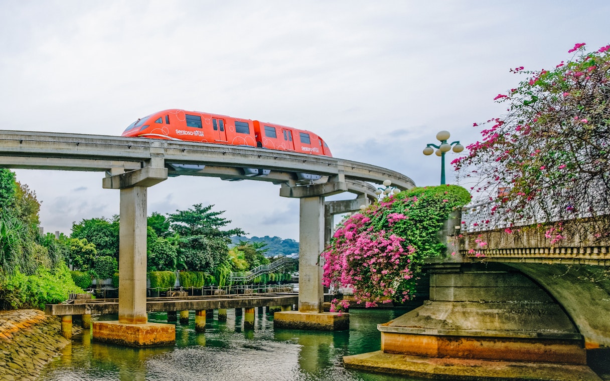 Monorail traveling over a bridge on Sentosa Island, Singapore, surrounded by lush greenery.