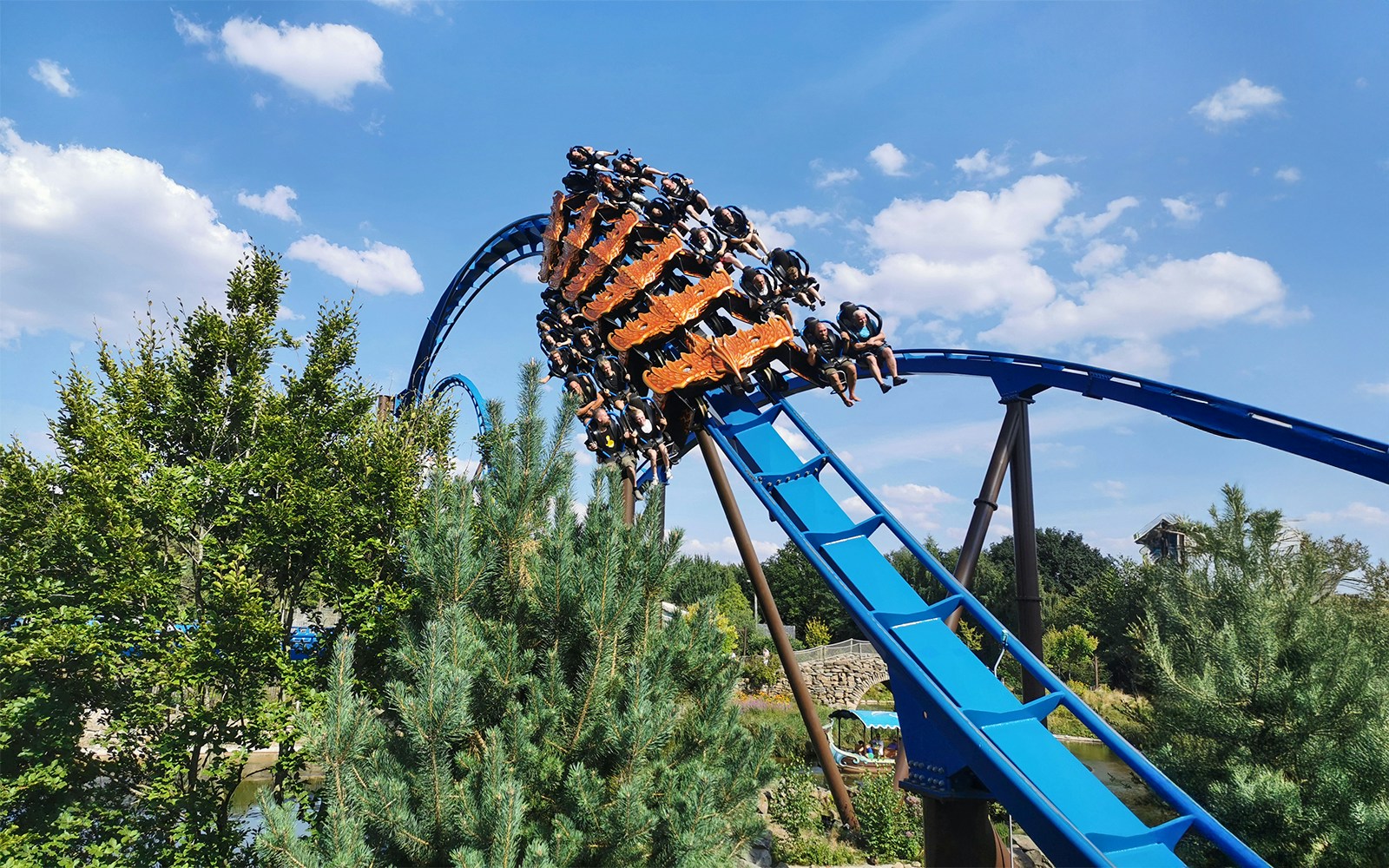 Roller coaster with riders on a blue track at a park, surrounded by trees.