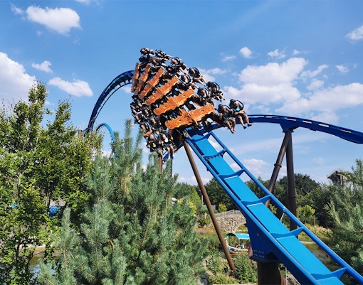 Roller coaster with riders on a blue track at a park, surrounded by trees.