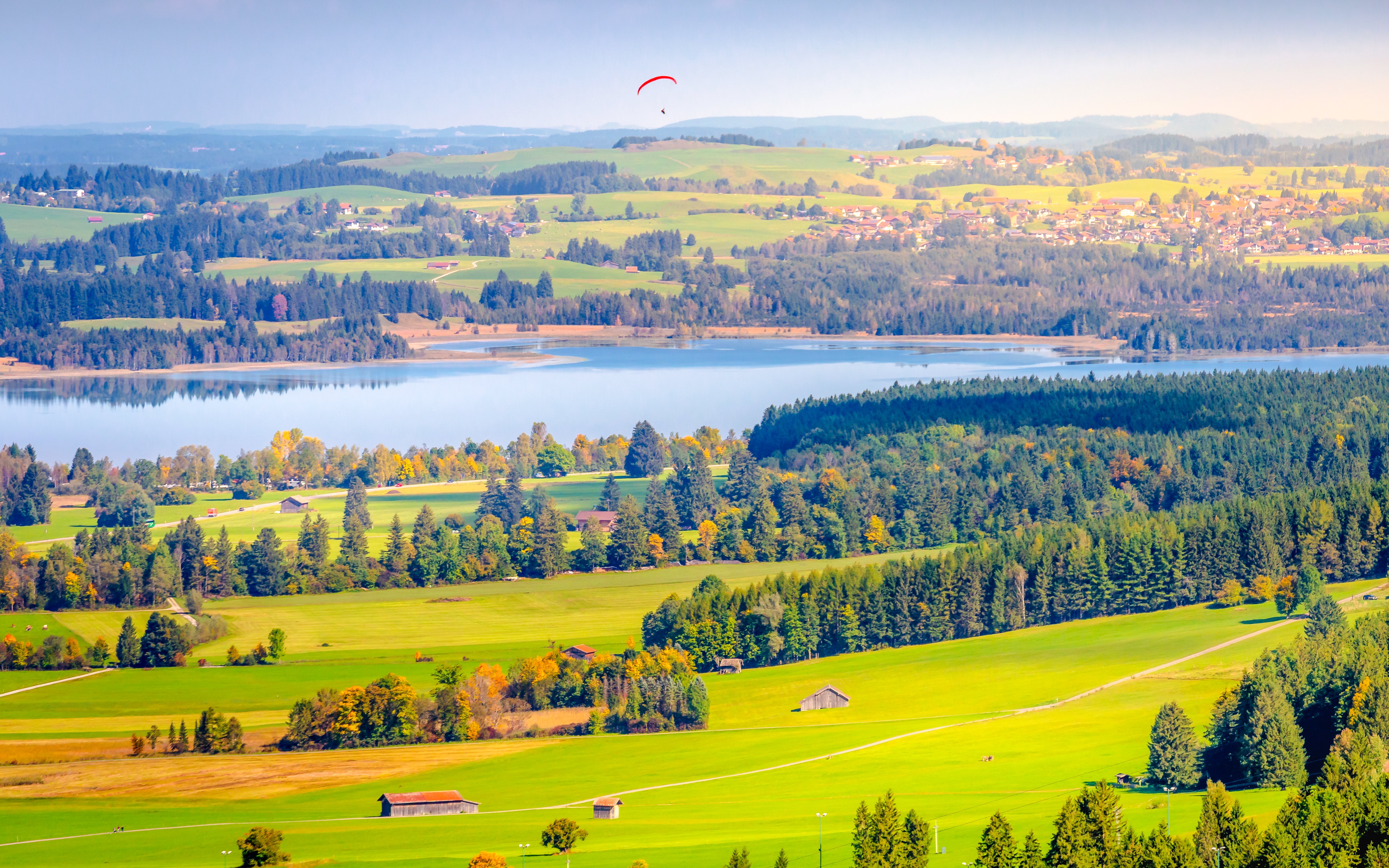 Aerial view of Schwangau Village with lush fields, forest, and a lake in the background.
