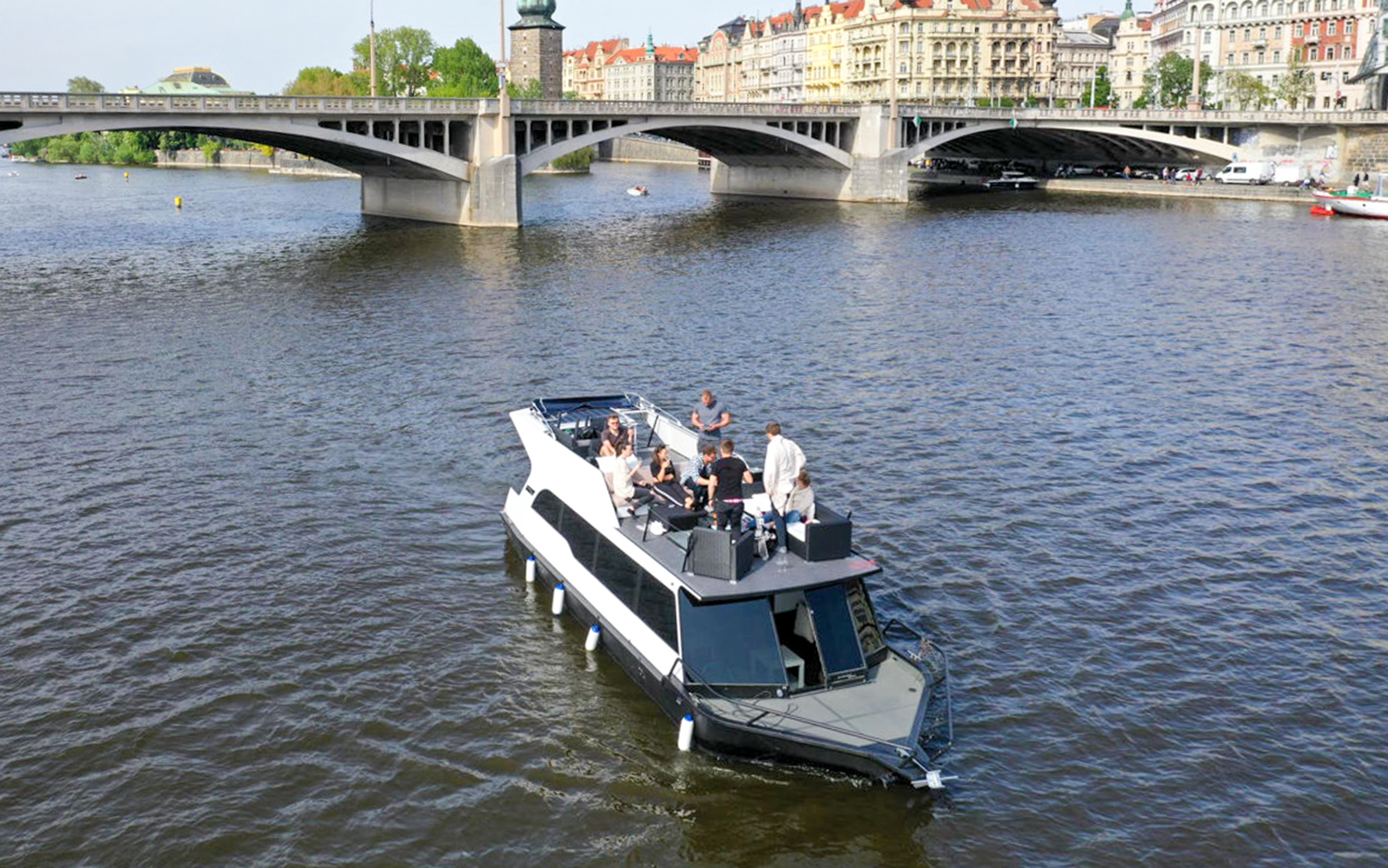 Prague river cruise on a yacht with people enjoying drinks near a historic bridge.