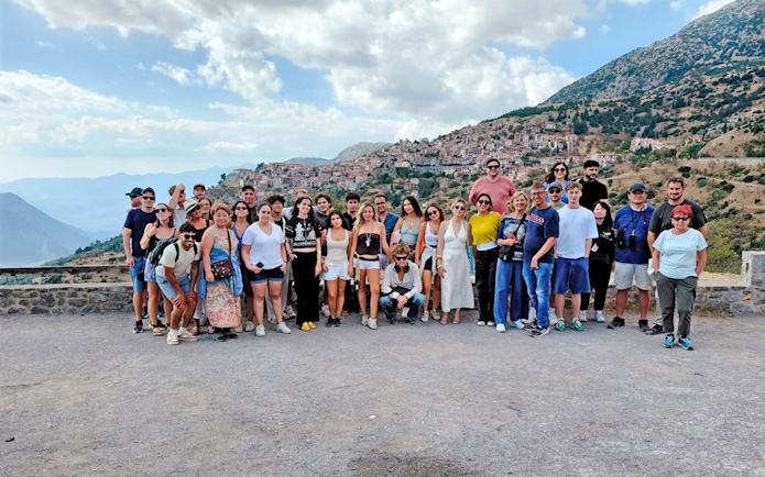 Tour group posing with a scenic view of a hillside village and mountains in the background.