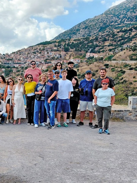 Tour group posing with a scenic view of a hillside village and mountains in the background.