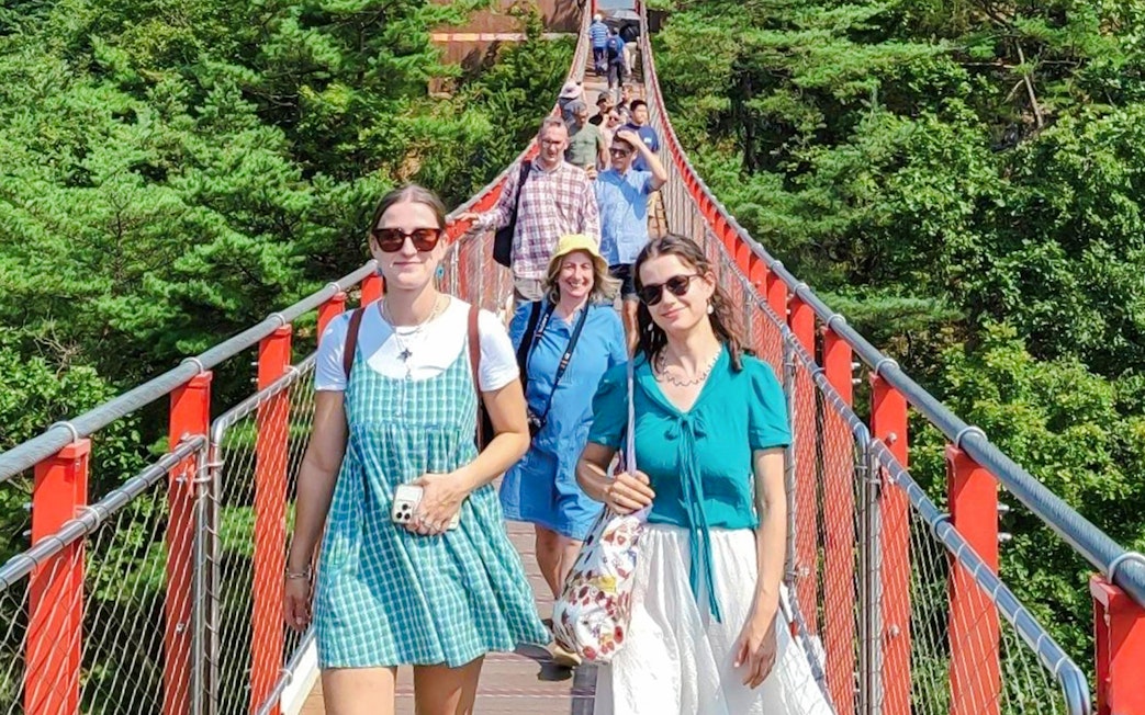 Tourists crossing a red suspension bridge over a forest on the DMZ tour.