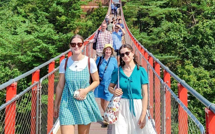 Tourists crossing a red suspension bridge over a forest on the DMZ tour.