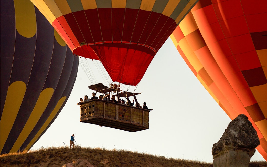 Hot air balloons with passengers floating over a hill at sunrise.