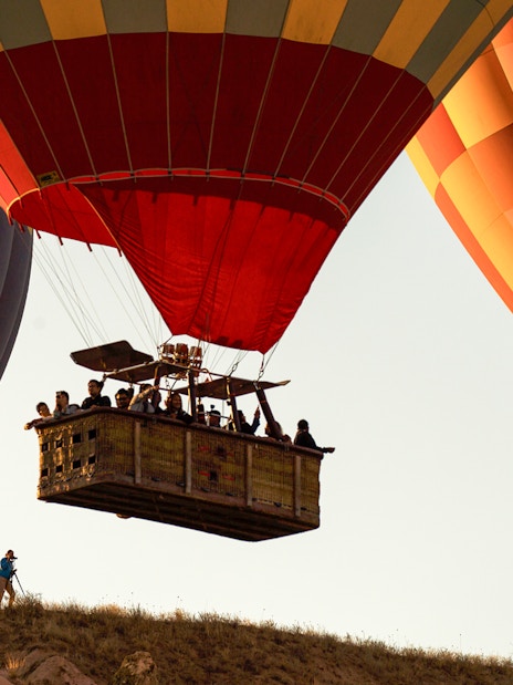 Hot air balloons with passengers floating over a hill at sunrise.