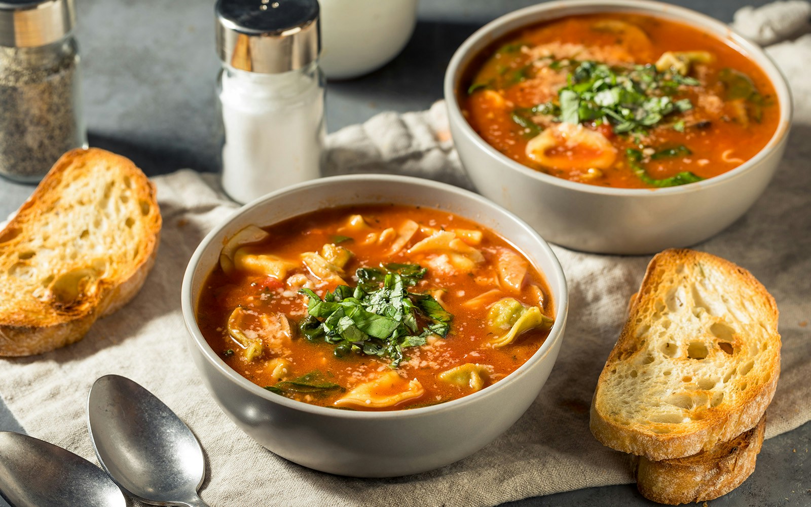 Tortellini soup with basil and parmesan, served with toasted bread, representing Mediterranean cuisine.