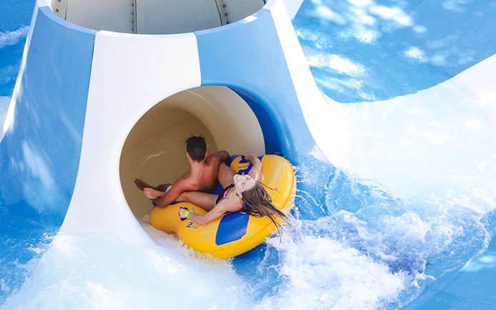 Two people on a yellow raft entering a water slide at Aquafan Water Park.