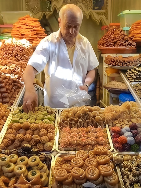 Vendor arranging traditional sweets at Jema el Fna street food market in Marrakesh.