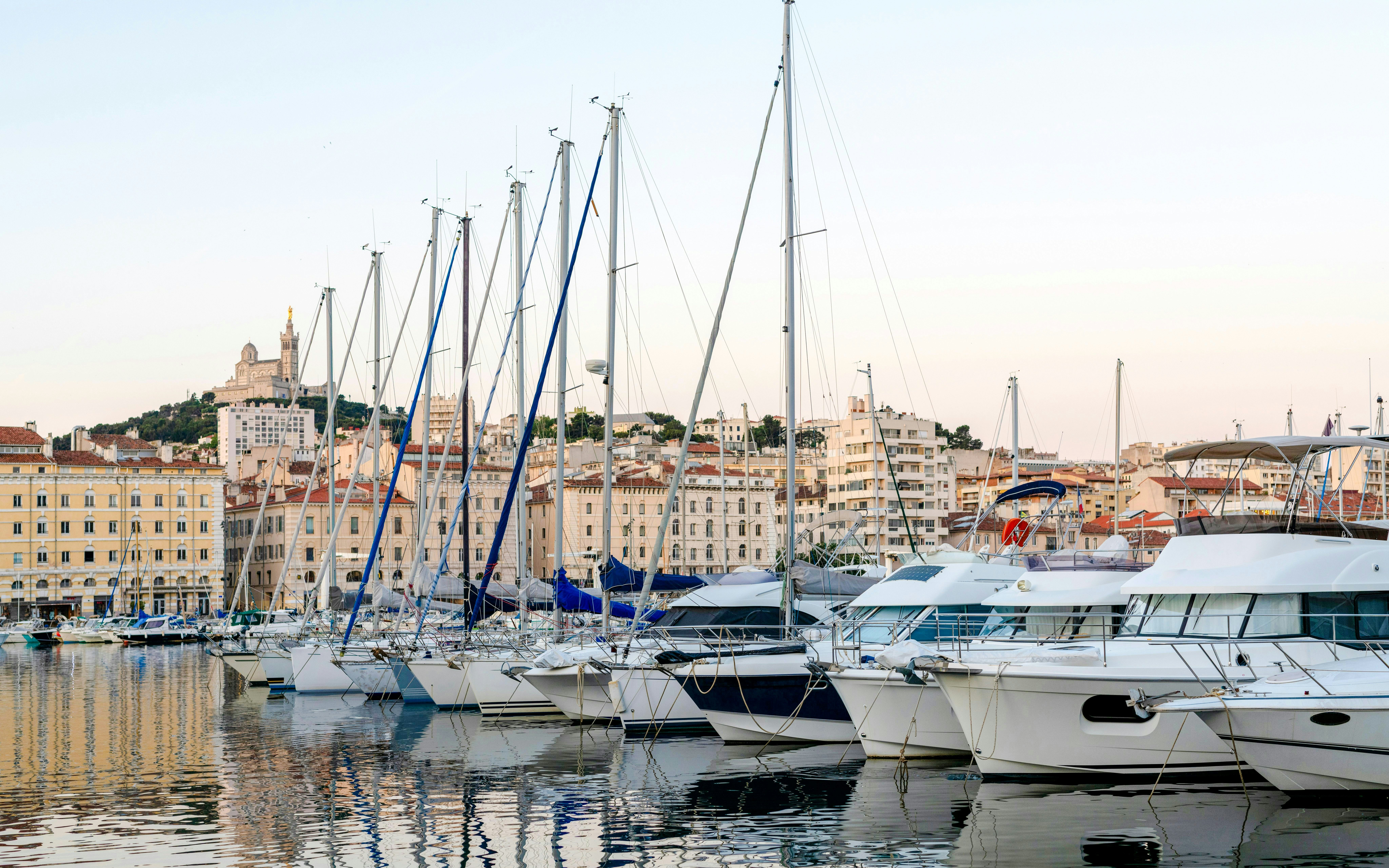 Sailboats docked at Vieux-Port Marseille with Notre-Dame de la Garde in the background.