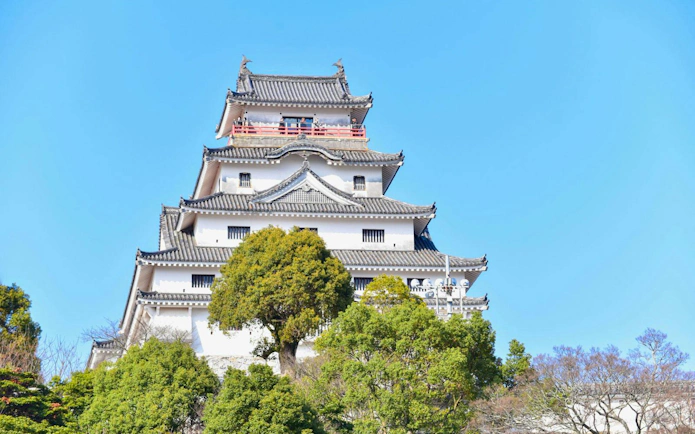 Karatsu Castle with traditional architecture surrounded by trees under a clear blue sky.