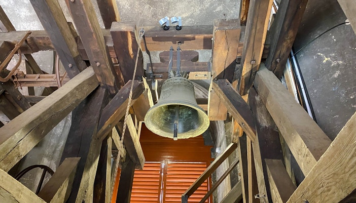 Bell inside St. Nicholas Bell Tower, Prague, surrounded by wooden beams.