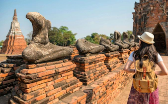 Traveler exploring ancient Ayutthaya temple ruins with headless Buddha statues, Thailand.