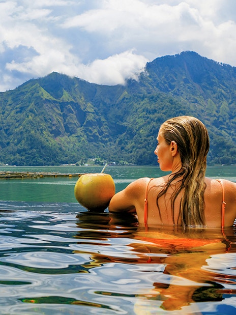 Woman relaxing in hot springs with Mount Batur view, Bali.