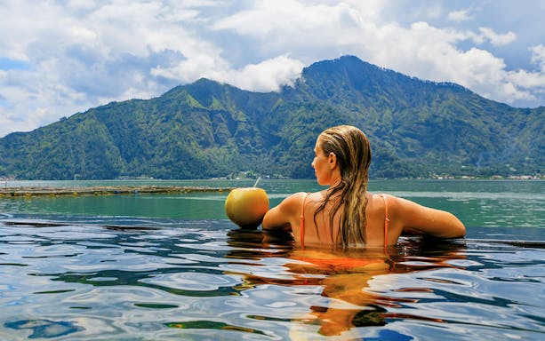 Woman relaxing in hot springs with Mount Batur view, Bali.