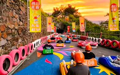 Visitors riding alpine slide carts at Huangteng Gorge, Guangzhou, with colorful track and sunset backdrop.