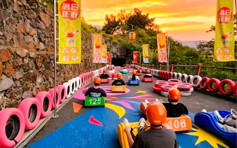 Visitors riding alpine slide carts at Huangteng Gorge, Guangzhou, with colorful track and sunset backdrop.