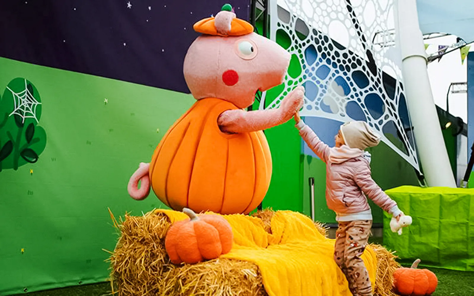 Child high-fiving Peppa Pig in pumpkin costume at Halloween event in Peppa Pig Park.
