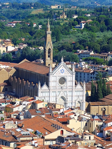 Aerial view of Santa Croce Basilica in Florence, Italy, surrounded by cityscape and greenery.