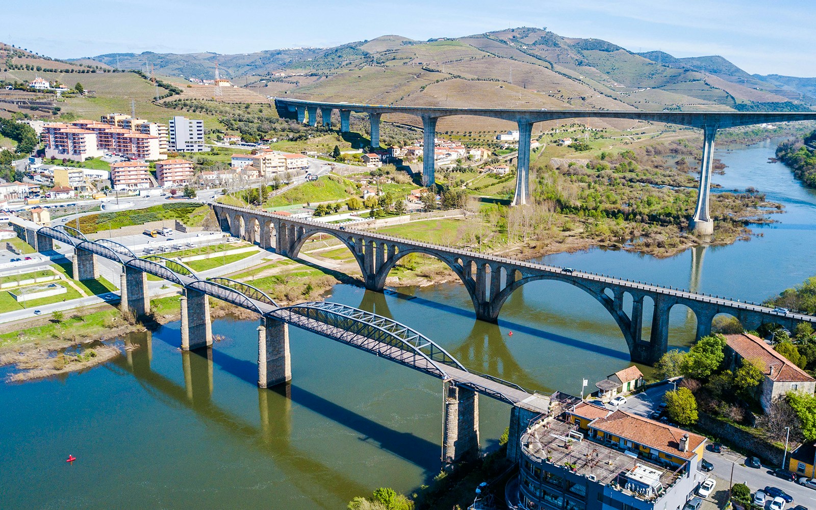 Bridges spanning the Douro River in Peso da Régua, Portugal, with surrounding hills and buildings.