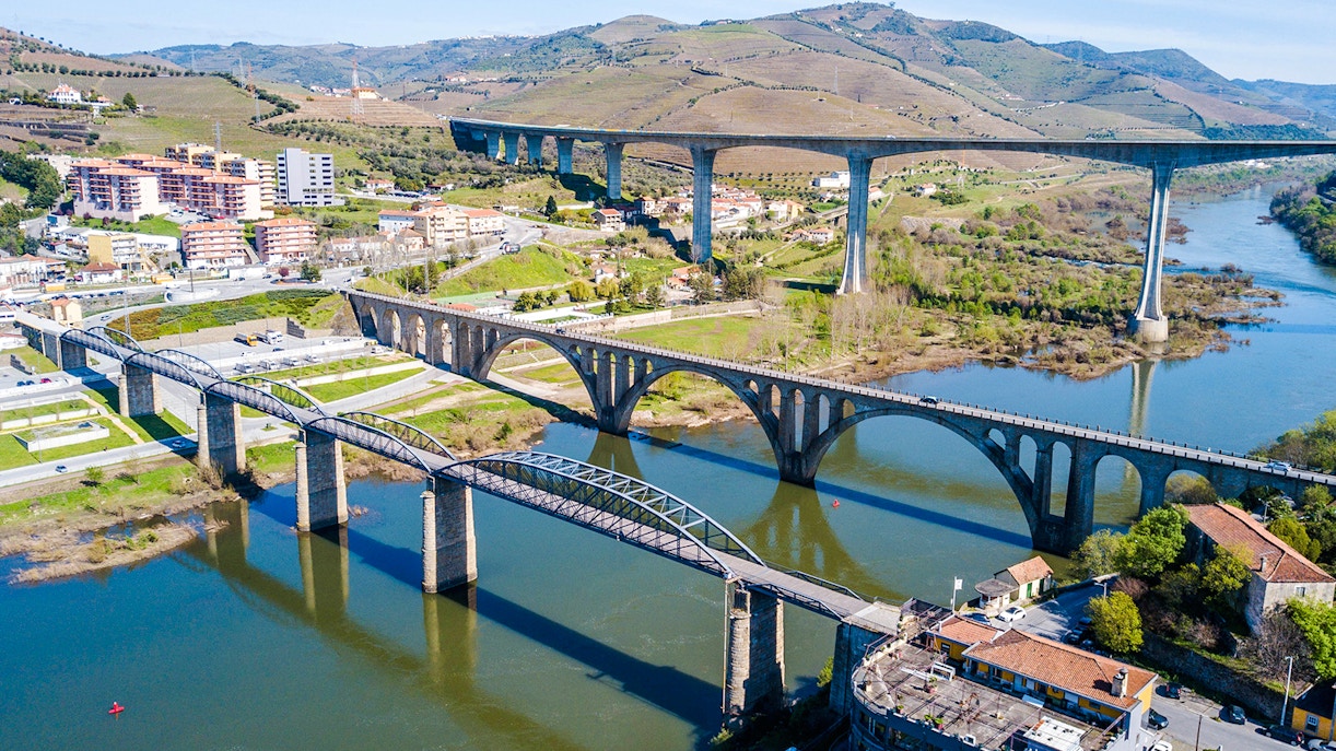 Bridges spanning the Douro River in Peso da Régua, Portugal, with surrounding hills and buildings.