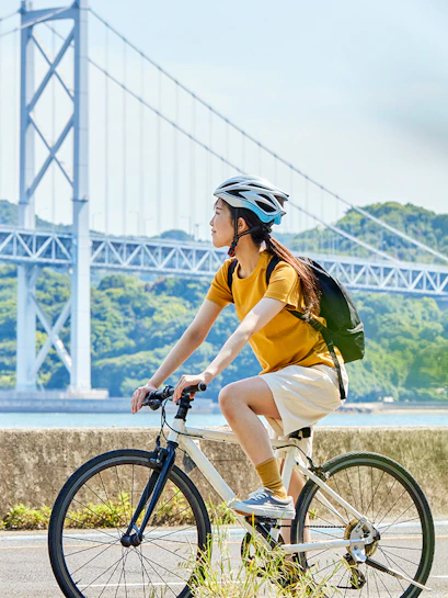 Cyclist riding near a large suspension bridge with lush hills in the background.