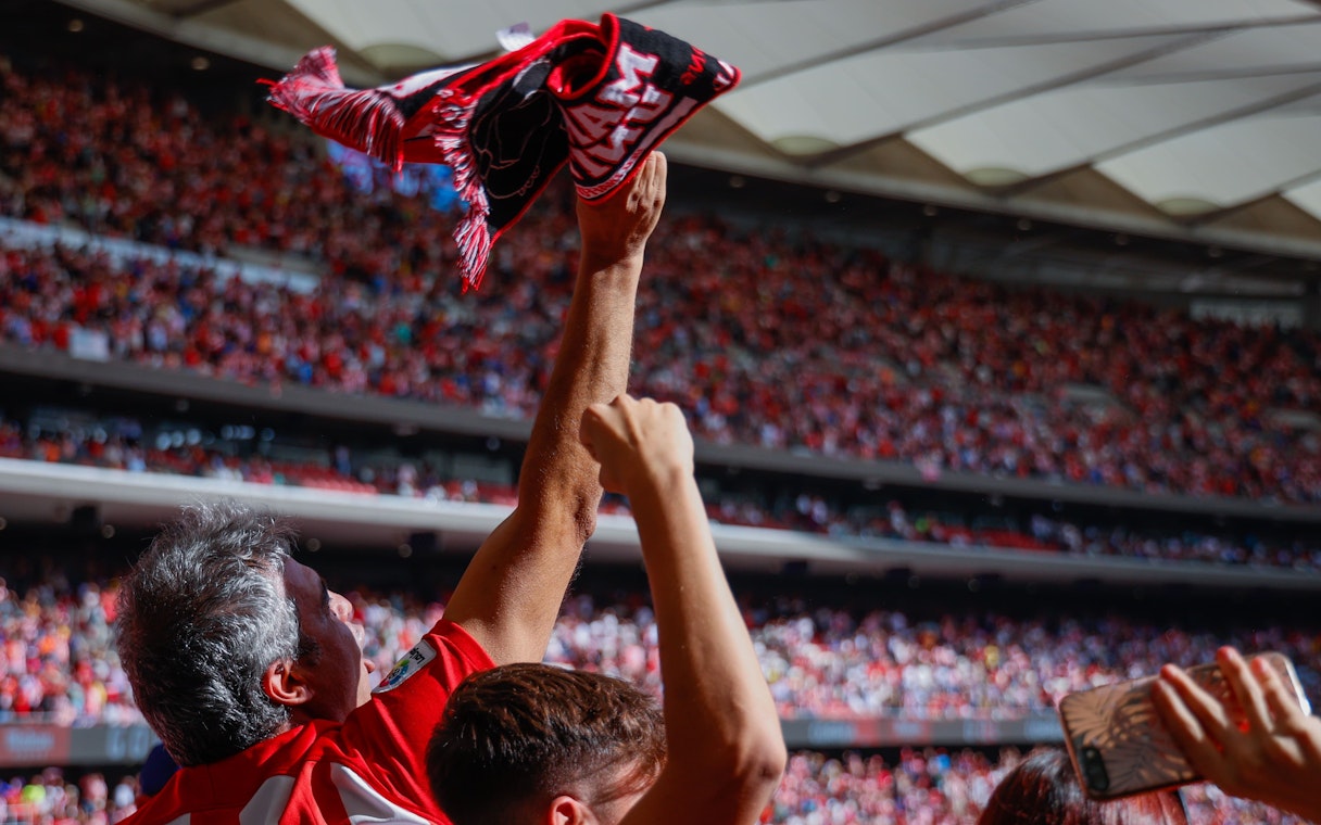 Crowd cheering with Atlético Madrid scarf at a packed stadium.