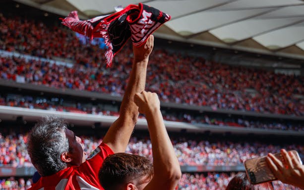 Crowd cheering with Atlético Madrid scarf at a packed stadium.