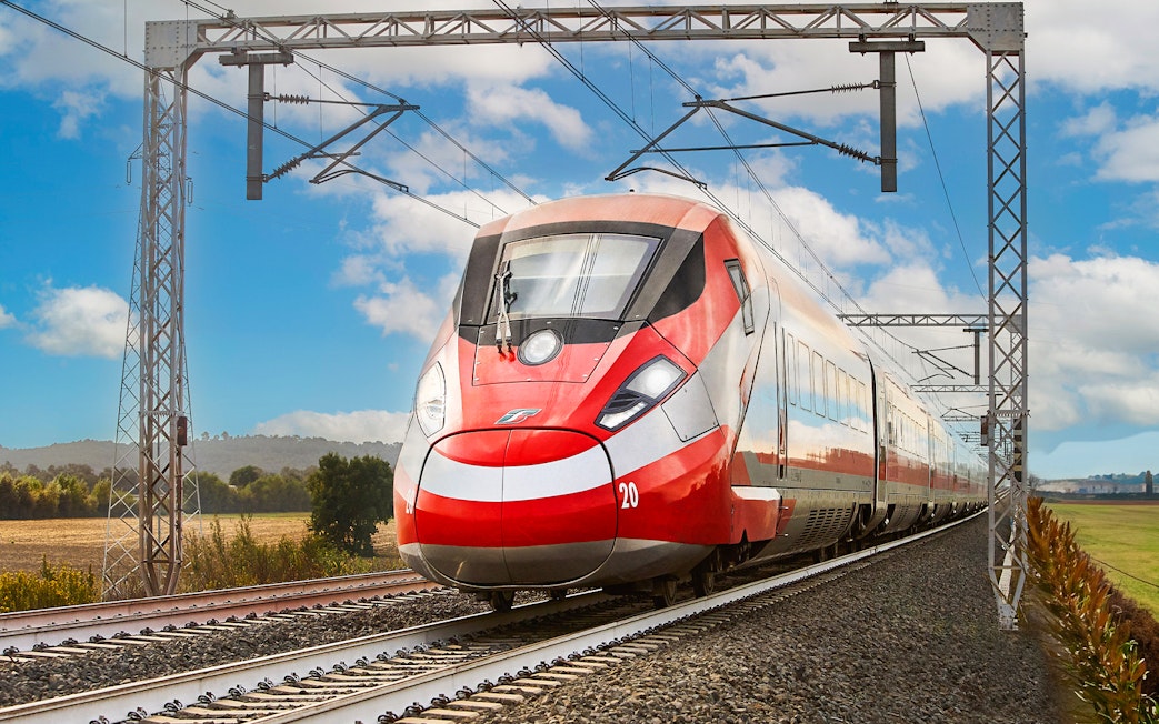 Trenitalia train traveling through Italian countryside under blue sky.