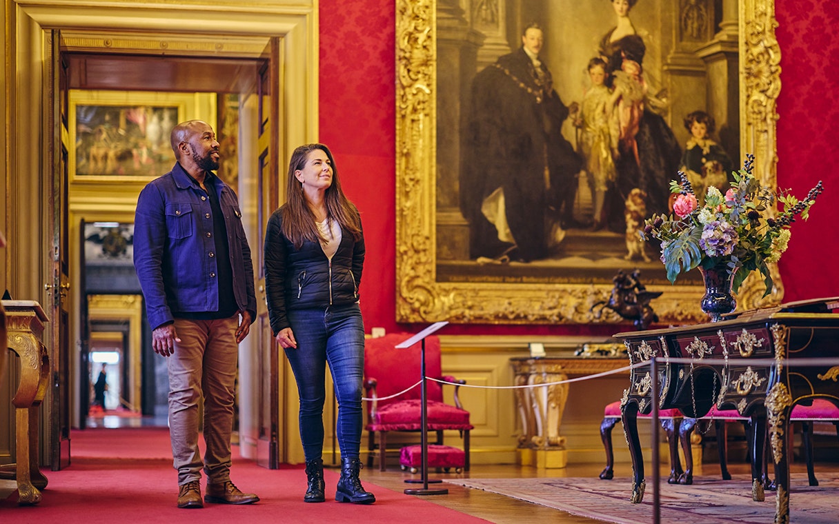 Visitors exploring the ornate State Rooms inside Blenheim Palace, featuring a large historical painting.