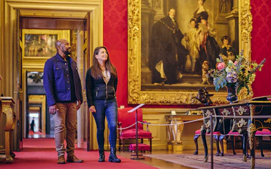Visitors exploring the ornate State Rooms inside Blenheim Palace, featuring a large historical painting.