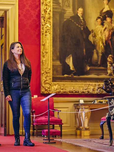Visitors exploring the ornate State Rooms inside Blenheim Palace, featuring a large historical painting.