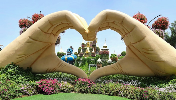Giant hand sculpture framing floral castle and genie at Dubai Miracle Garden.