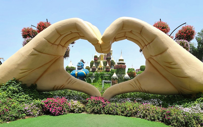 Giant hand sculpture framing floral castle and genie at Dubai Miracle Garden.
