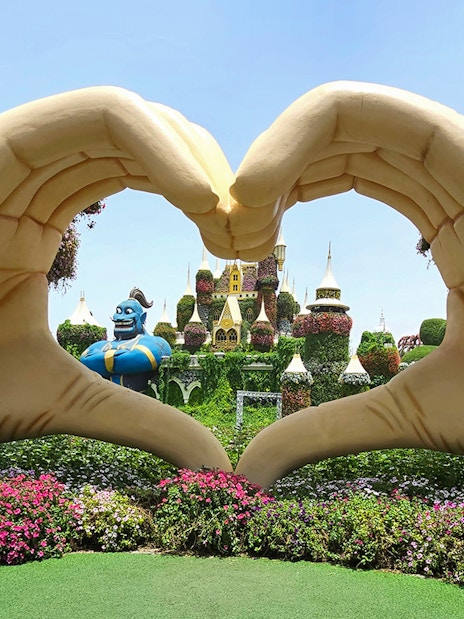 Giant hand sculpture framing floral castle and genie at Dubai Miracle Garden.