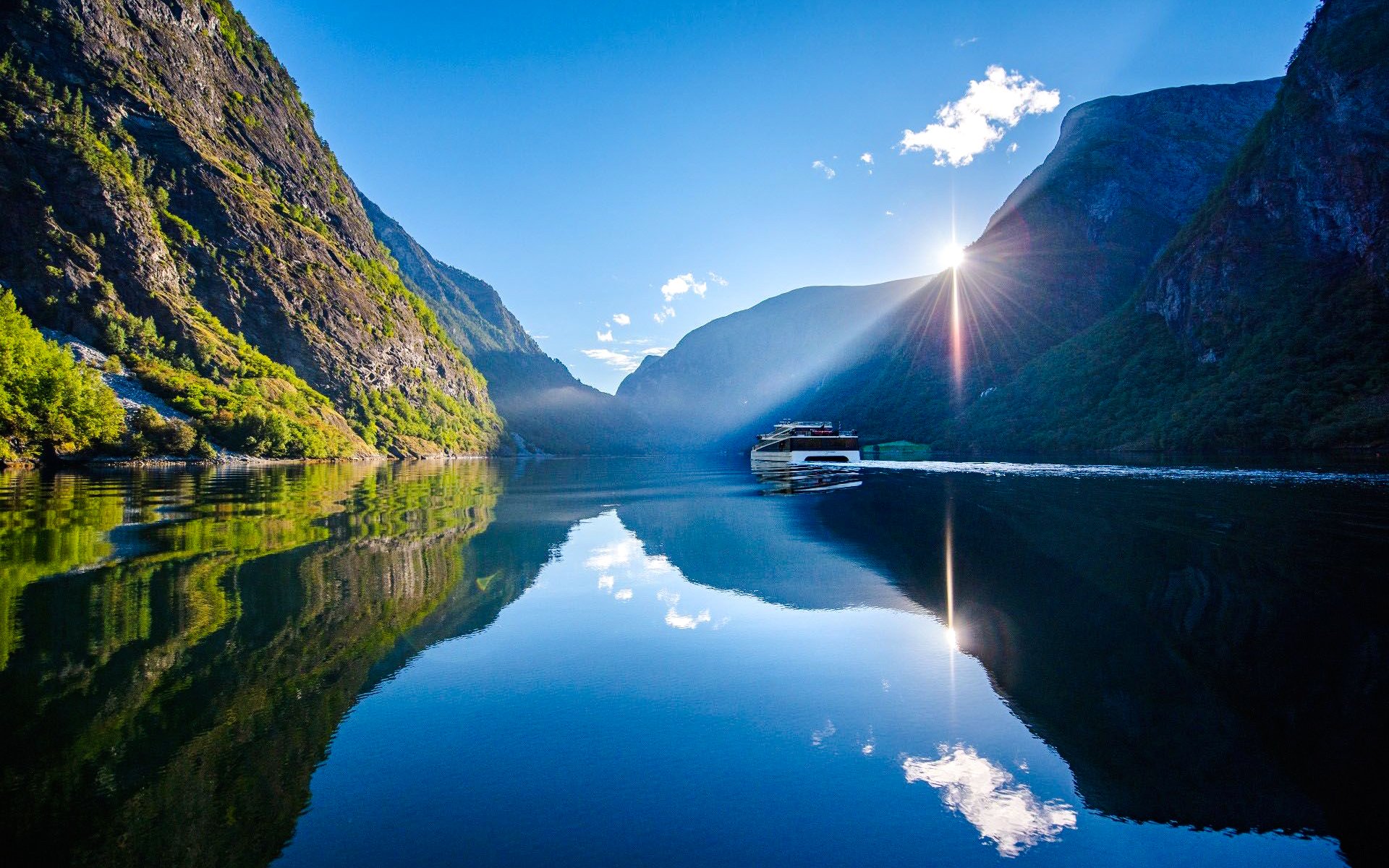 Boat cruising through Naeroyfjorden Fjord with sunlit mountains and clear reflections.