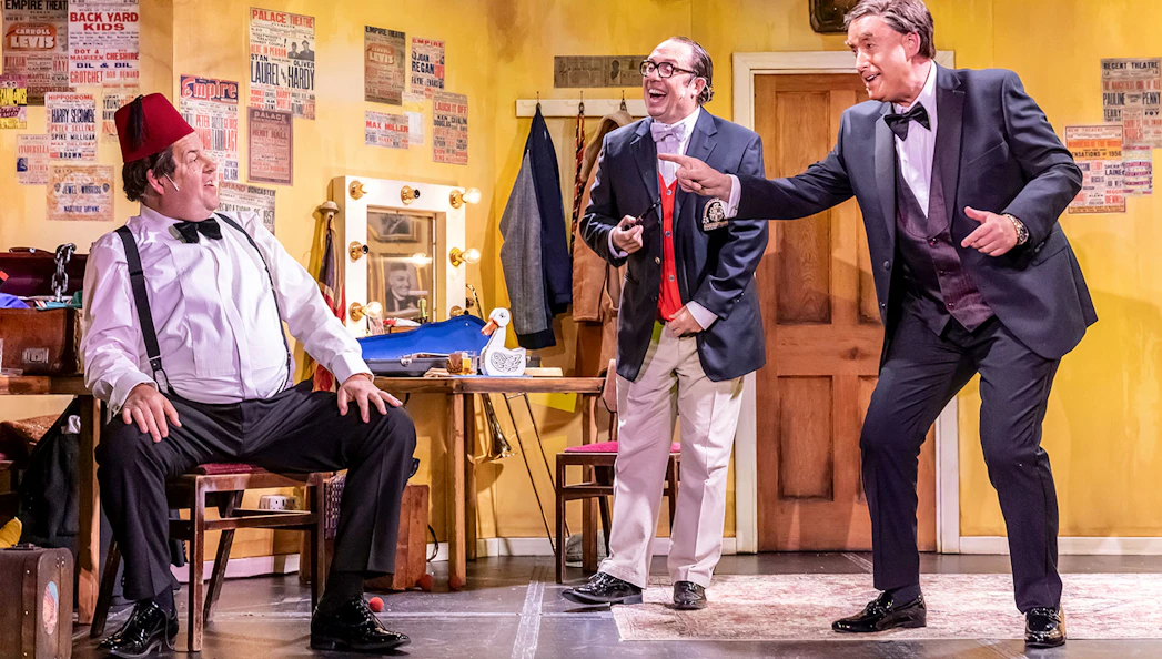 Three actors in a comedic scene on stage, set in a vintage dressing room, for "The Last Laugh" show.