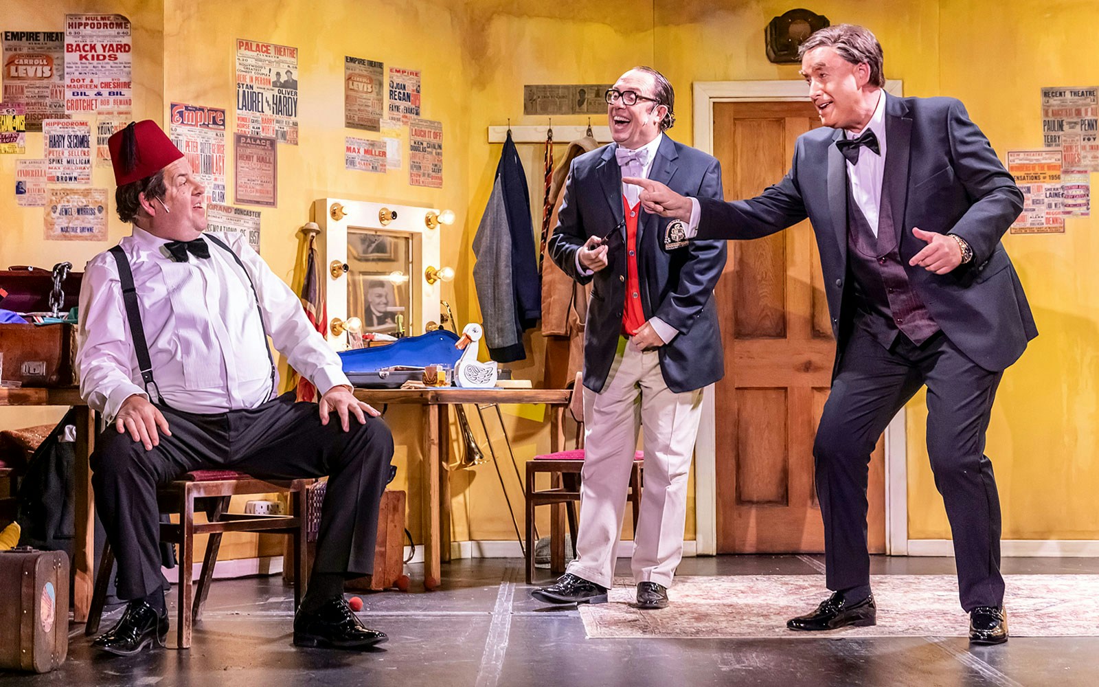 Three actors in a comedic scene on stage, set in a vintage dressing room, for "The Last Laugh" show.
