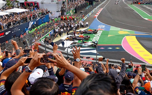 Crowd cheering at Formula 1 Mexico Grand Prix with race cars on track.