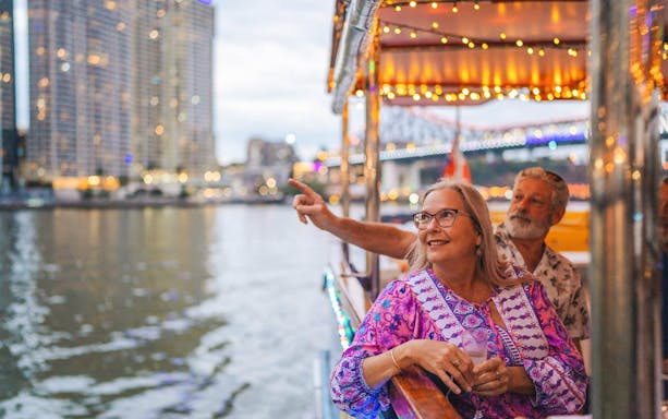 Couple enjoying Brisbane River cruise at dusk with city lights in the background.