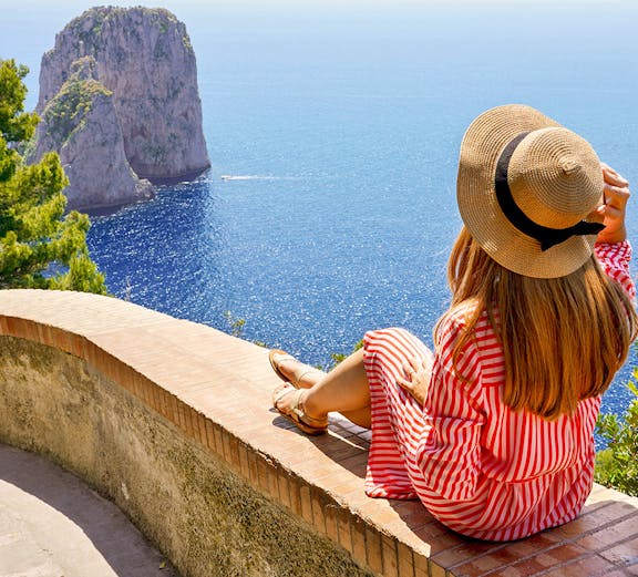 Woman sitting on a wall overlooking the sea and Faraglioni rock formations, Capri.
