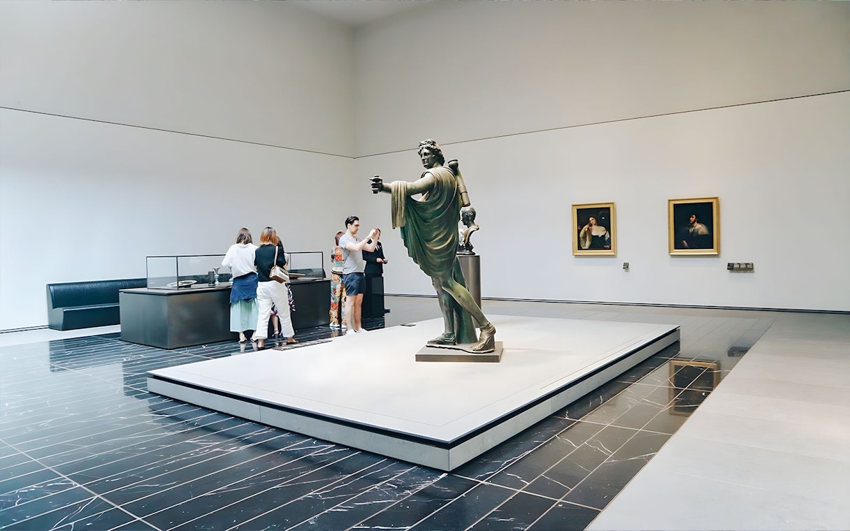 Museum visitors viewing a classical statue and paintings.