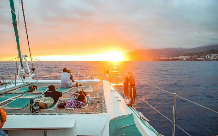Catamaran at sunset in Madeira with passengers watching the ocean.