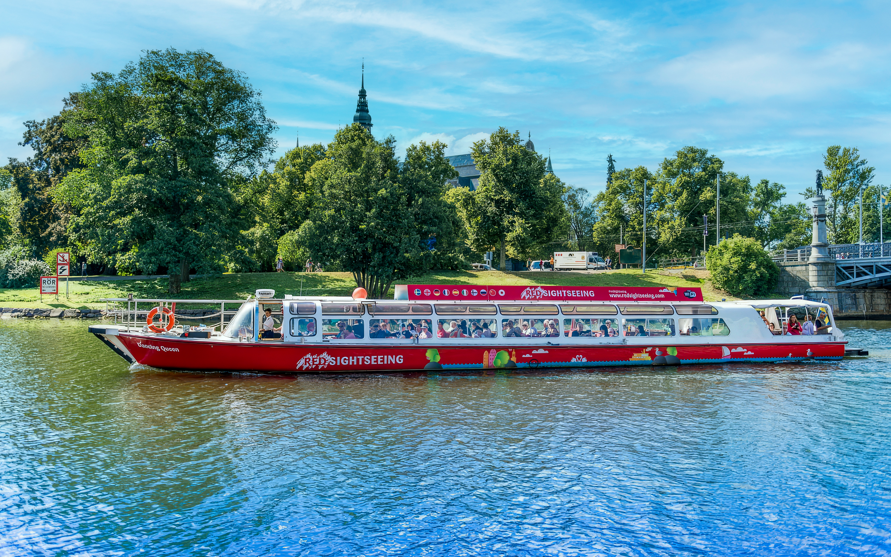 Sightseeing boat on a canal in Stockholm, Sweden with lush greenery in the background.