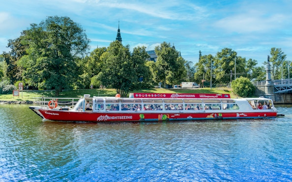 Sightseeing boat on a canal in Stockholm, Sweden with lush greenery in the background.