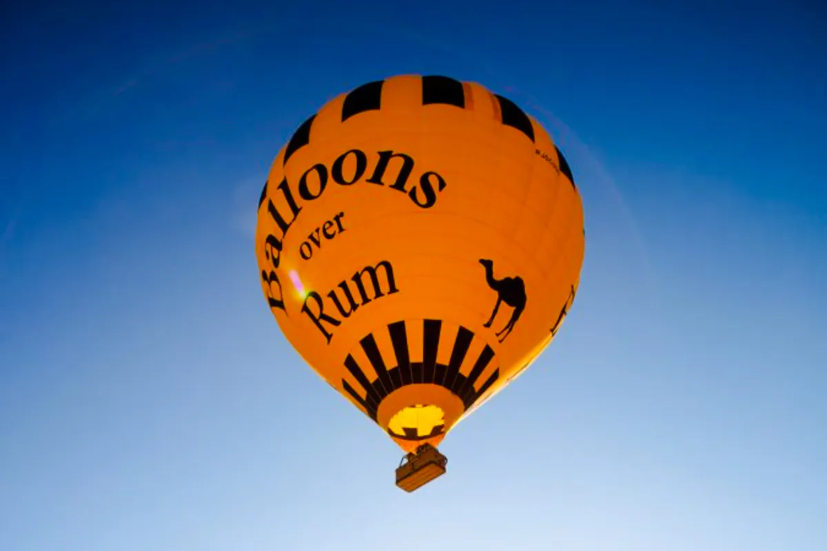 Hot air balloon with "Balloons over Rum" text in Wadi Rum sky.