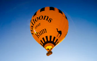 Hot air balloon with "Balloons over Rum" text in Wadi Rum sky.