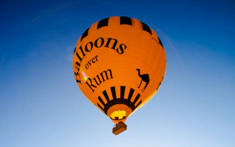 Hot air balloon with "Balloons over Rum" text in Wadi Rum sky.