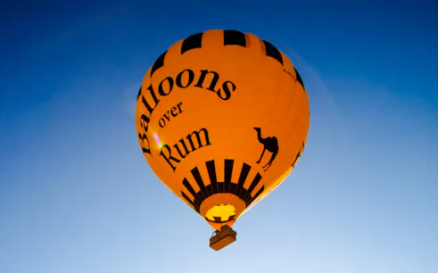 Hot air balloon with "Balloons over Rum" text in Wadi Rum sky.